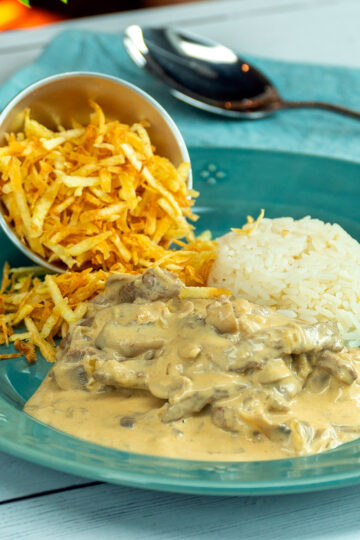 Rindergeschnetzeltes Stroganoff mit Reis und knusprigen Kartoffelstreifen auf einem Teller angerichtet.