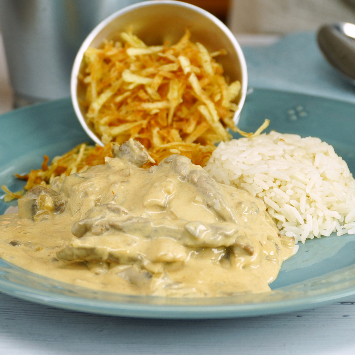 Serviertes Rindergeschnetzeltes Stroganoff mit Reis und knusprigen Kartoffelstreifen.