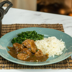 Schweinewürfel in Schwarzbiersauce mit Reis und grünem Gemüse serviert.