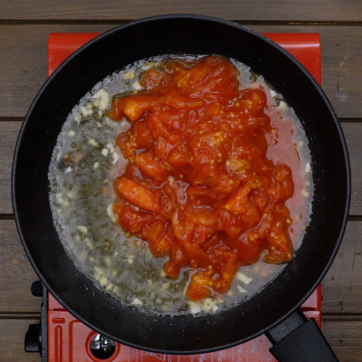 Tomaten und Weißwein werden in der Pfanne zur Sauce gekocht.